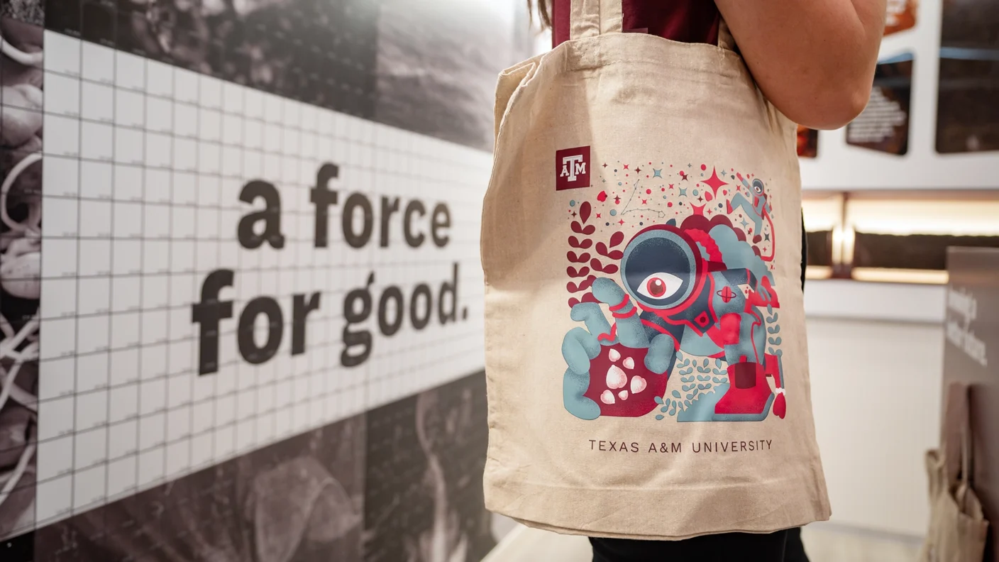 Person carrying a Texas A&M branded and designed tote bag in front of the "a force for good" mosaic wall at SXSW 2025.