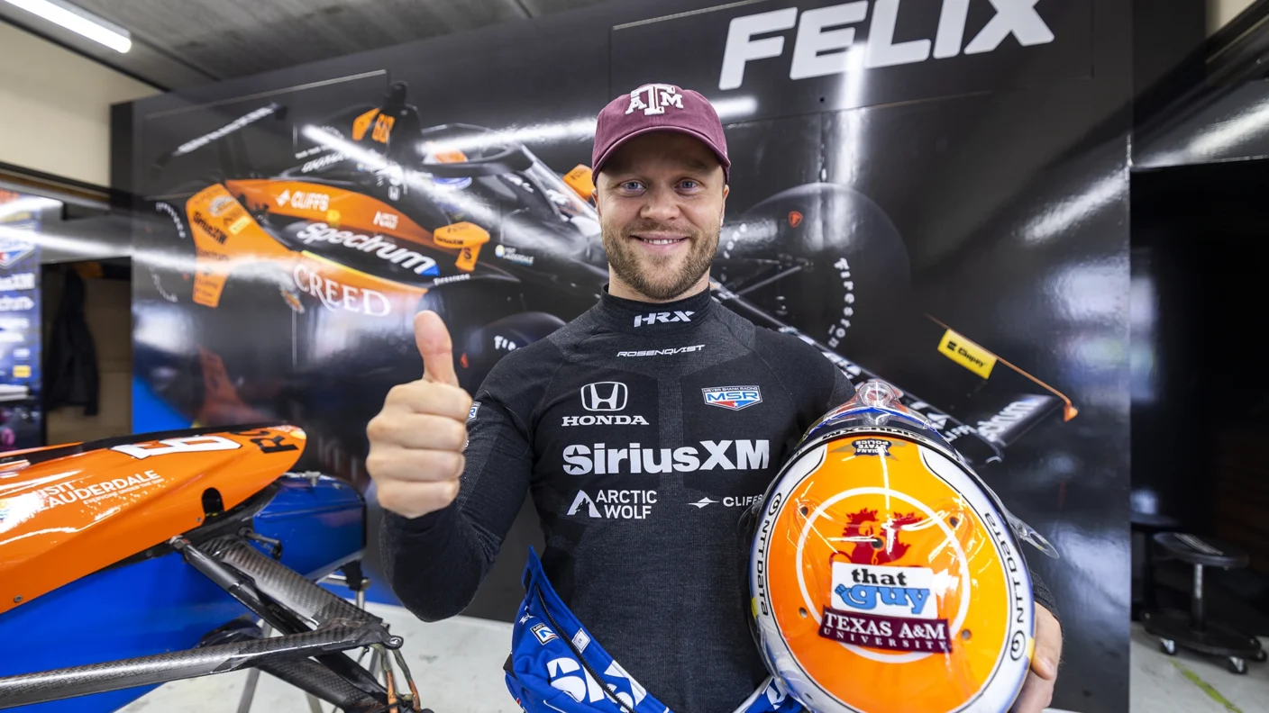 IndyCar driver stands with a Texas A&M hat on and a Texas A&M branded helmet