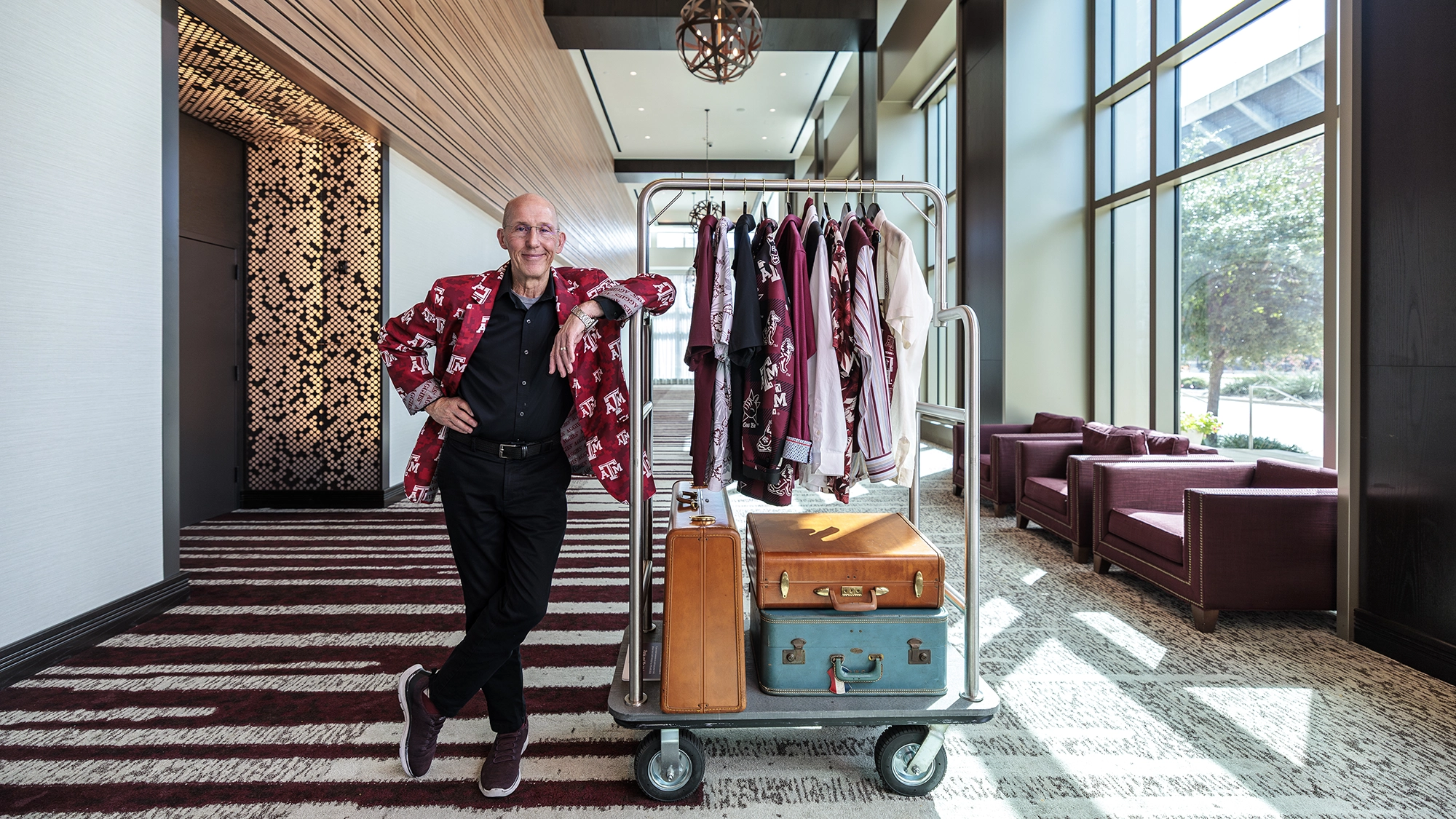 Texas A&M Hotel and Conference Center frontman, Sean Artman wearing a Texas A&M branded suit jacket and leaning against a luggage rack