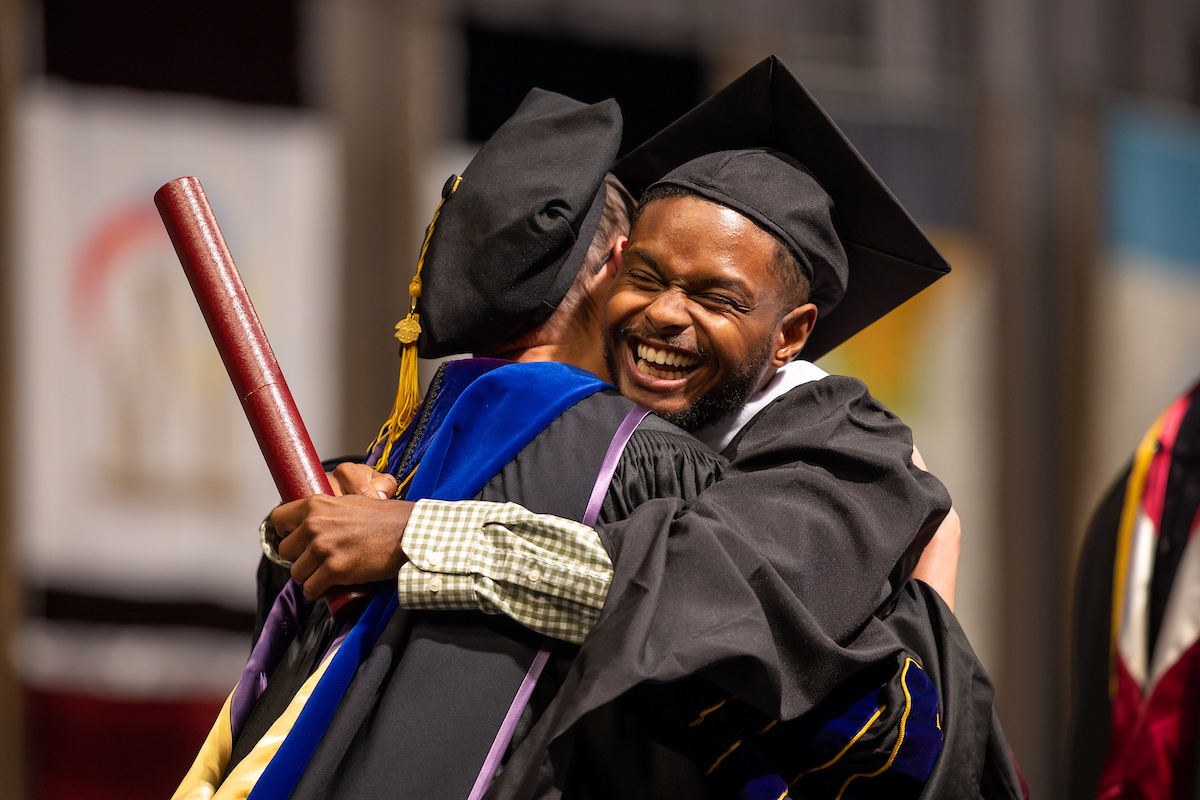 Student hugs their professor with their diploma in hand as they walk across the stage at Texas A&M graduation